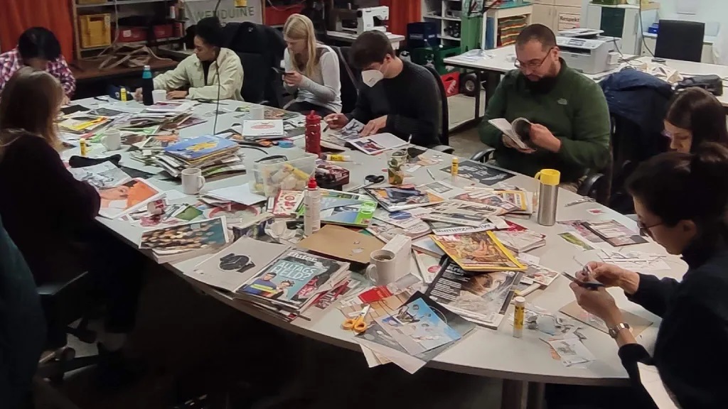 Menschen sitzen an einem Tisch mit vielen Magazinen und machen Collage.